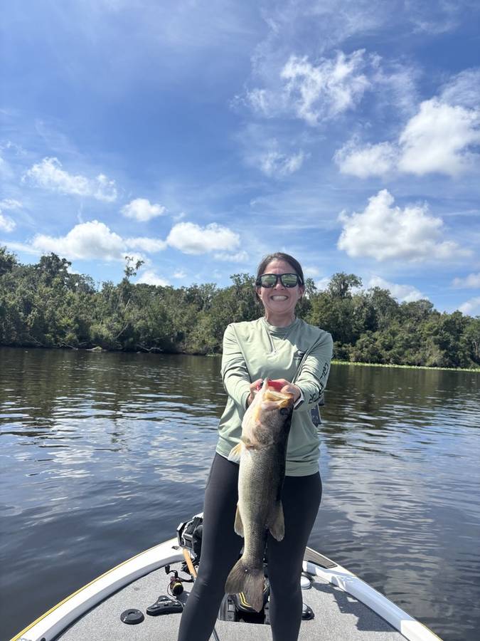 Jen holding up a heavy bass along the cypress-lined bank